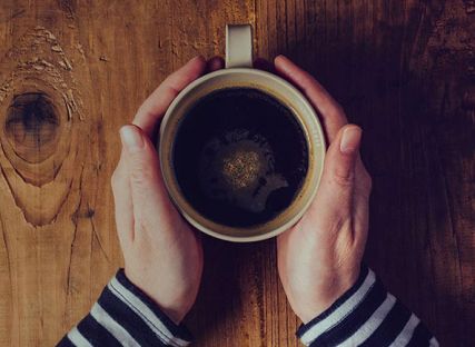 cup of coffee on table with woman's hands around it